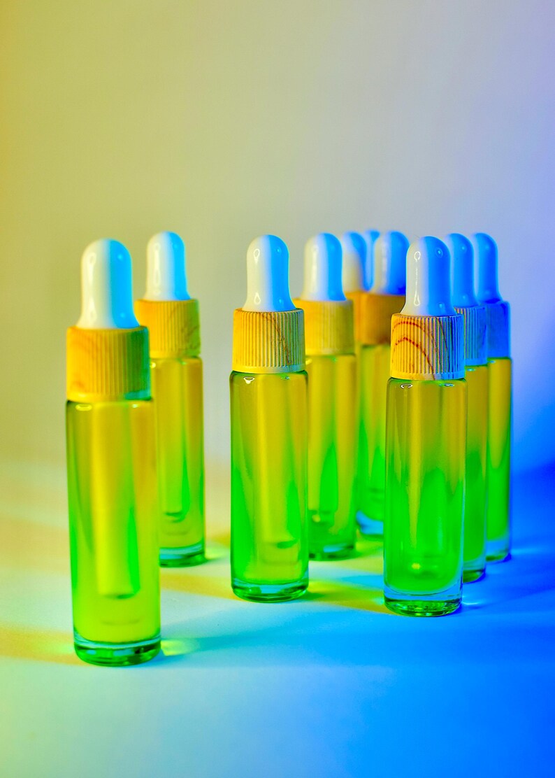 May include: A collection of clear glass dropper bottles filled with a vibrant green liquid. Each bottle has a white and blue dropper top with a yellow wooden collar. The bottles are arranged on a gradient background of yellow and blue.