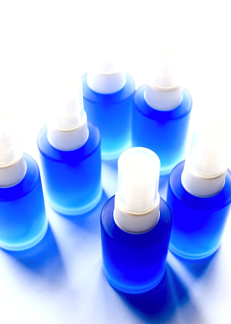 May include: Six small blue spray bottles with white tops. The bottles are arranged in a circle on a white surface.