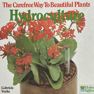 May include: A book cover with the title "The Carefree Way To Beautiful Plants" and the word "Hydroculture" in green. A potted plant with red flowers and green leaves is in the foreground. A clear tube with a cork stopper is in the pot.