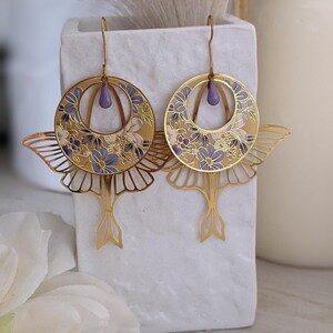 May include: Gold tone earrings with a floral design and a purple teardrop accent. The earrings are shaped like butterflies with delicate wings.