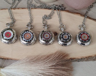 May include: Five silver pocket watch necklaces with different colorful mandala designs. The necklaces are displayed on a wooden surface.