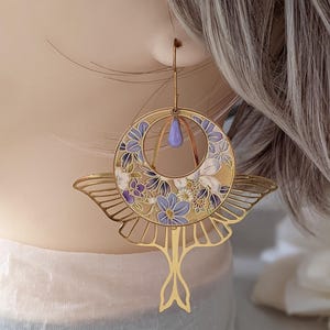 May include: Gold earrings with a floral design and a butterfly shape. The earrings are decorated with purple and white flowers on a gold background.