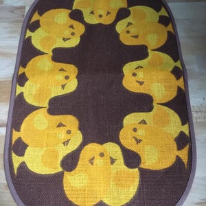 May include: An oval-shaped brown and yellow rug with a repeating pattern of stylised yellow birds. The birds are arranged in a circle around the centre of the rug.