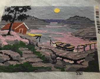 May include: A needlepoint canvas with a partially completed design of a house, a tree, and a lake with a yellow sun in the sky. The canvas has a number 337 printed on it.