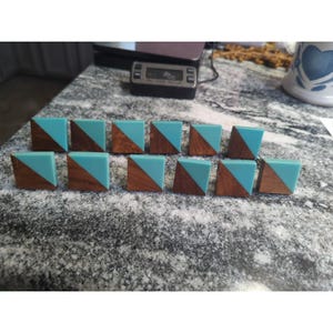 May include: Ten square cabinet knobs are displayed. Each knob has a diagonal split design, with a turquoise blue resin section and a brown wood section. The knobs are arranged on a speckled grey surface.