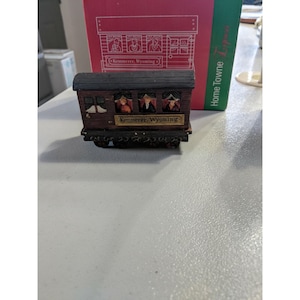 May include: A miniature brown train car with the text "Kemmerer, Wyoming" on the side. The train car has small windows with figures inside. The roof is dark brown, and the wheels are black.