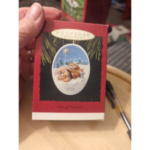 Könnte beinhalten: Eine rote Hallmark Keepsake Ornament Schachtel mit einer ovalen Illustration von einem Fuchs, einem Hasen und einer Maus im verschneiten Wald unter einem Stern. Der Text lautet Keepsake Ornament, 1993 und Star of Wonder auf dunklem Grund.