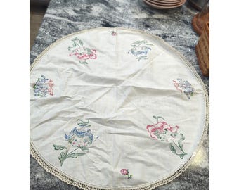 Centro de mesa con tapete de lino vintage, flores estampadas y caras de duendes infantiles.