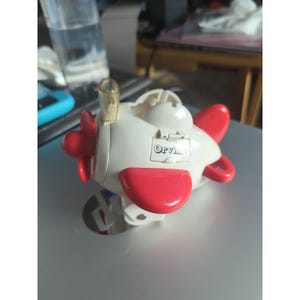 May include: A white and red toy airplane with a propeller and wings. The toy has the word "Orvis" printed on the side. The airplane is sitting on a silver surface.