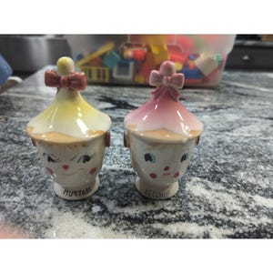 May include: A set of three ceramic mugs with a speckled, matte finish. The mugs are in shades of cream, light gray, and dark gray. Each mug has a simple, minimalist design and a rounded handle.