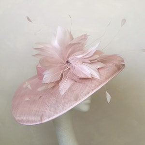 Op de afbeelding: Een roze hoed met een brede rand en een grote roze verenversiering.