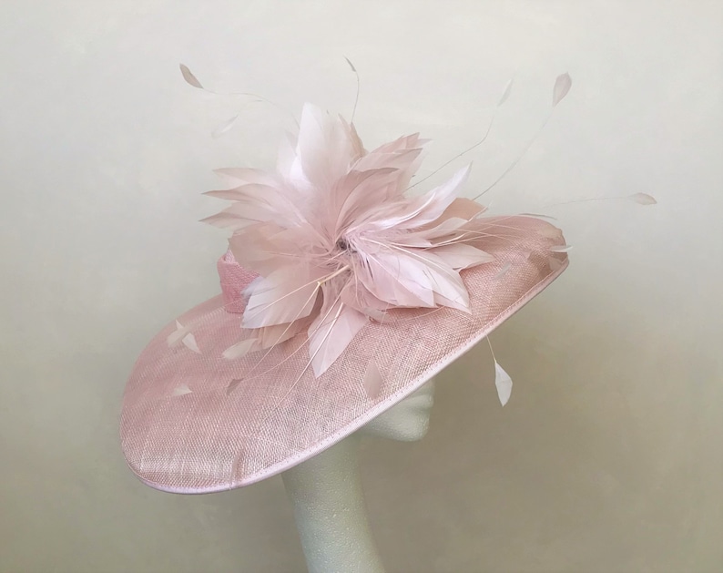 Op de afbeelding: Een roze hoed met een brede rand en een grote roze verenversiering.