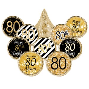 Puede incluir: Pegatinas doradas y negras para la fiesta de cumplea&ntilde;os n&uacute;mero 80. Las pegatinas presentan una variedad de dise&ntilde;os, incluyendo un patr&oacute;n de rayas blancas y negras, brillo dorado y el n&uacute;mero 80. El texto en las pegatinas incluye "Feliz cumplea&ntilde;os n&uacute;mero 80", "Brindis por 80 a&ntilde;os" y "80&ordm;".