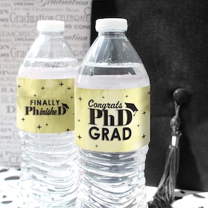 May include: Two clear plastic water bottles with gold and black labels. The labels have the text "Congrats PhD Grad" and "Finally PhinisheD".
