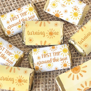 May include: A set of small, yellow and white gift tags with a sun design and the text "First Trip Around the Sun" and "Turning One".