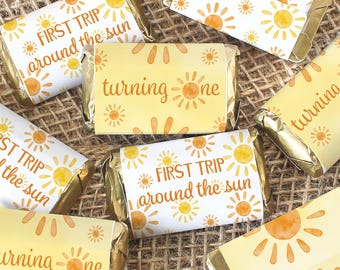 May include: A set of small, yellow and white gift tags with a sun design and the text "First Trip Around the Sun" and "Turning One".