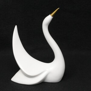 May include: White ceramic swan figurine with a gold beak, the swan is in a graceful pose with its neck curved back.
