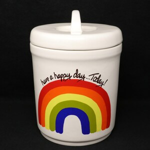 May include: White ceramic canister with a lid and a rainbow design. The canister has the text "have a happy day...Today!" written on it.