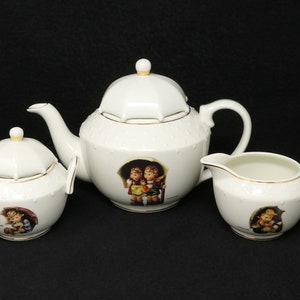 May include: A white porcelain tea set with a teapot, sugar bowl, and creamer. Each piece features a whimsical illustration of children under an umbrella.