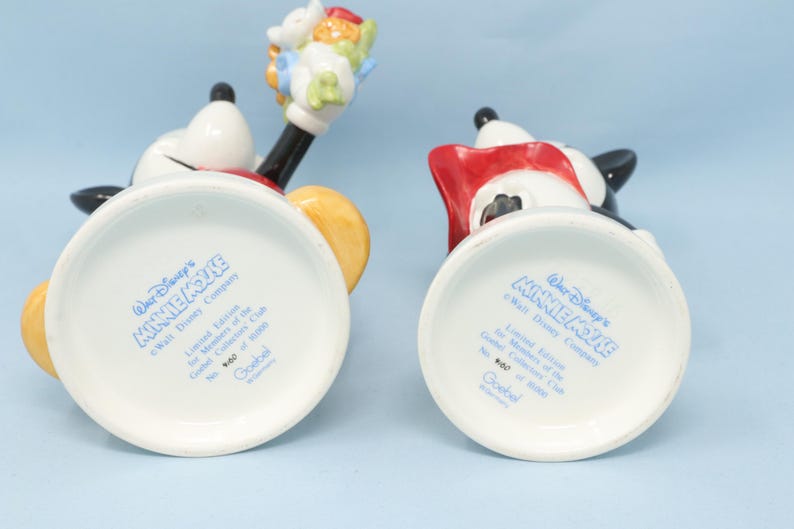 Puede incluir: Dos figuras de cer&aacute;mica de Minnie Mouse, una con flores. Las figuras son blancas, negras, rojas y amarillas. La parte inferior de cada figura tiene el texto "Walt Disney's MINNIE MOUSE".