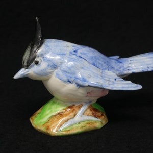 May include: A blue and white ceramic bird figurine with a black crest. The bird is perched on a green and brown base.