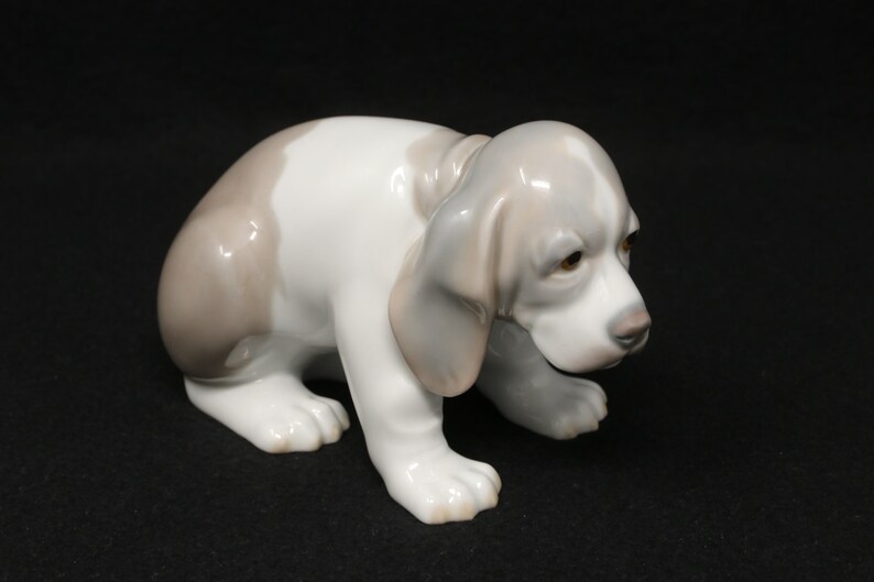 May include: A porcelain figurine of a white and grey puppy with brown eyes. The puppy is sitting on its hind legs with its front paws extended forward.