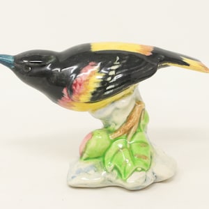 May include: A ceramic figurine of a black and yellow bird perched on a branch with green leaves. The bird has a red breast and is painted in a realistic style.