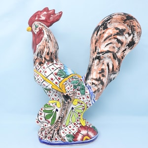May include: A ceramic rooster figurine with a red comb, yellow beak, and patterned body. The body features a white base with red dots, green leaves, and yellow accents. The tail has brown and black brushstrokes.