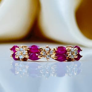 May include: A gold band ring with a row of ruby and diamond stones. The ring is set in a pave setting.