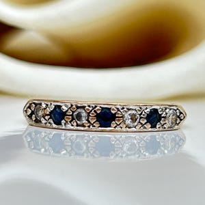 May include: A gold band ring with a row of alternating blue sapphires and white diamonds. The ring has a delicate, intricate design.
