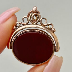 Può includere: Un portachiavi girevole dorato con una pietra di corniola rossa. Il portachiavi ha un design decorativo e ornato.