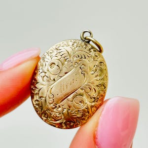Può includere: Medaglione ovale in oro con un motivo floreale inciso e la parola "Maria" su uno stendardo.