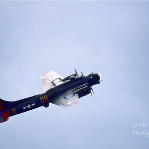 May include: A black and silver World War II era bomber plane flies in a clear blue sky. The plane has a red, white, and blue star on the side and the letters "OR" on the fuselage.
