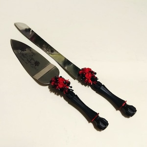 K&ouml;nnte beinhalten: Ein schwarzes und rotes Hochzeitstortenmesser-Set mit floralem Design. Das Messer tr&auml;gt die Gravur "The Beginning of Forever" auf der Klinge.