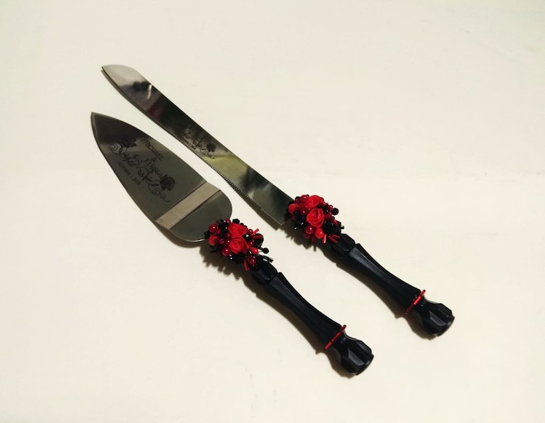 K&ouml;nnte beinhalten: Ein schwarzes und rotes Hochzeitstortenmesser-Set mit floralem Design. Das Messer tr&auml;gt die Gravur "The Beginning of Forever" auf der Klinge.