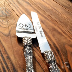 Pode incluir: Um conjunto de faca para cortar bolo de prata com uma pega decorativa e strass. A faca tem o texto "Mr. & Mrs. Beglarian 12.22.2018" gravado. O servidor tem o texto "Nanette & Armen 12.22.2018" e uma letra "B" em uma coroa gravada.