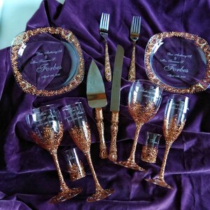 May include: A wedding set with two champagne flutes, two wine glasses, a cake knife, two forks, and two small shot glasses. All the glasses and the cake knife are decorated with gold accents. The plates are engraved with the names "Rev. Anthony D. & Mrs. Jasmine J. Forbes" and the date "April 11th, 2020".