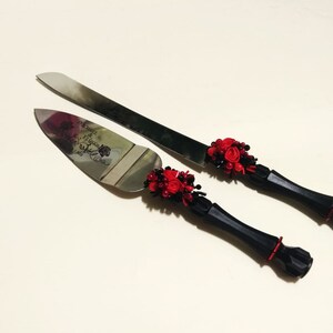 K&ouml;nnte beinhalten: Ein schwarzes und rotes Hochzeitstortenmesser-Set mit einem dekorativen Griff und dem eingravierten Text "Mr. & Mrs." auf der Klinge.