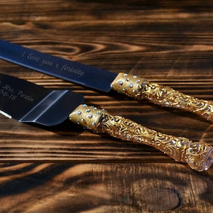 May include: A cake knife and server set with gold-colored handles and engraved blades. The knife reads "I love you x forinity" and the server reads "Mr. & Mrs. Partin 10-6-18". The handles have a decorative pattern and are adorned with small blue accents.