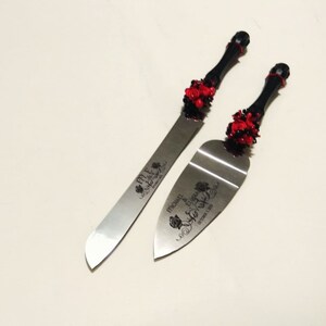 K&ouml;nnte beinhalten: Ein schwarzes und rotes Hochzeitstorten-Schneideset mit einer silbernen Klinge und einem schwarzen Griff, der mit roten Rosen verziert ist. Die Klinge ist mit dem Text "Mr. & Mrs. Michael & Eugenia October 1, 2016" graviert.