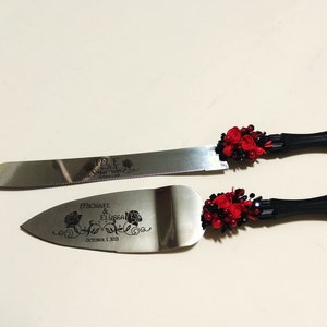 K&ouml;nnte beinhalten: Ein schwarzes und rotes Hochzeitstortenmesser-Set mit floralem Design und dem Text "Michael & Elyssa October 1, 2011".
