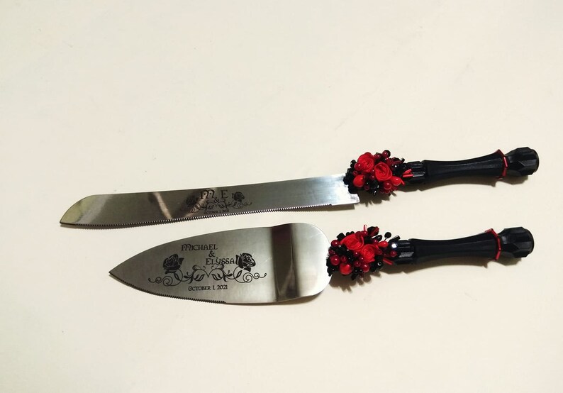 K&ouml;nnte beinhalten: Ein schwarzes und rotes Hochzeitstortenmesser-Set mit floralem Design und dem Text "Michael & Elyssa October 1, 2011".