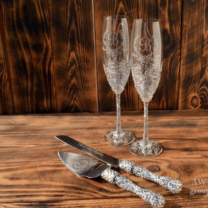 Pode incluir: Duas ta&ccedil;as de champanhe prateadas com um design floral e a letra "B" gravada na frente. Uma faca de bolo prateada com um design floral e uma al&ccedil;a de strass.