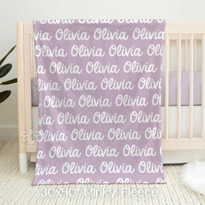 May include: A lavender-colored minky fleece blanket with the name "Olivia" repeated in white cursive lettering. The blanket is 30 inches by 40 inches.