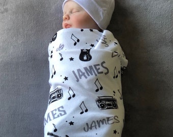 Może przedstawiać: Biały otulacz z czarno-szarym motywem muzycznym. Otulacz zawiera nuty muzyczne, gitarę, magnetofon i imię "JAMES" powtarzające się na całej powierzchni.