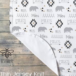 May include: White baby blanket with a black and white geometric pattern, brown and gray bears, and the name "Miles" repeated throughout. The blanket is made of thin jersey knit.