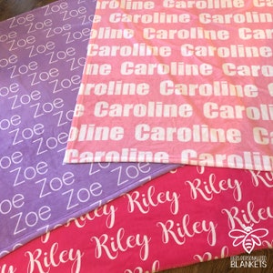 May include: Three personalized fleece blankets with different names. The top blanket is purple with the name "Zoe" repeated in white. The middle blanket is pink with the name "Caroline" repeated in white. The bottom blanket is pink with the name "Riley" repeated in white.