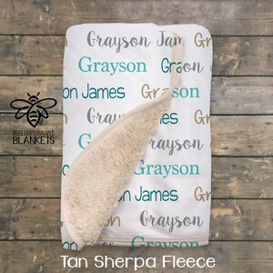 May include: White baby blanket with the name "Grayson" repeated in different colors and fonts. The blanket is made of tan sherpa fleece.