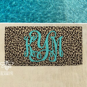 May include: A beach towel with a leopard print pattern and a turquoise monogram in the center. The monogram is the letters "KM".
