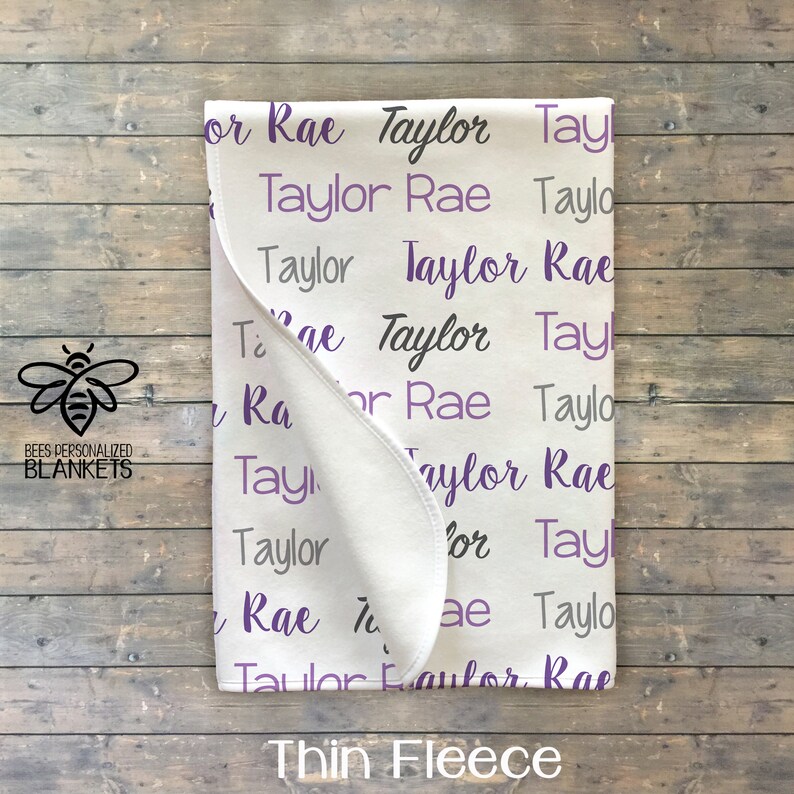 May include: White thin fleece baby blanket with the names "Taylor Rae" repeated in a purple and gray pattern.